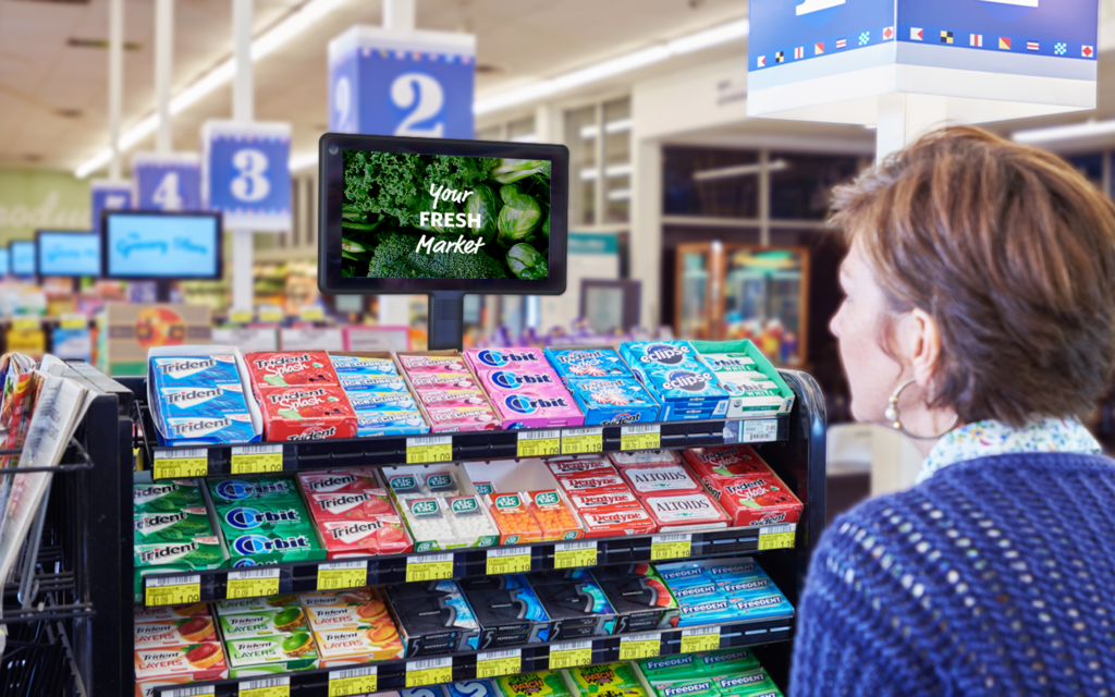 Woman reads a DOOH advertisement at a grocery store checkout.