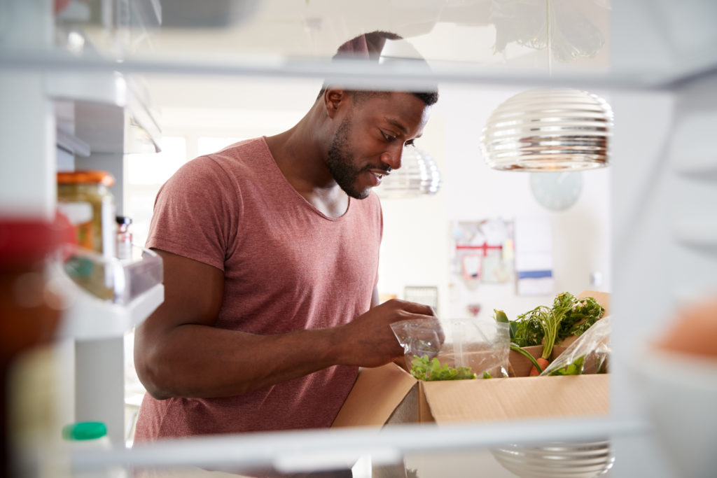 A man checks out his box of delivered groceries as he puts them in his fridge.