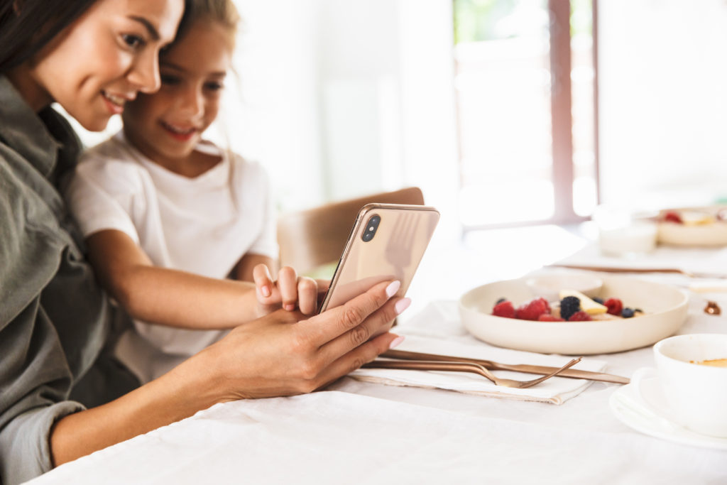 Image of a mother and daughter looking at a phone screen while sitting down at the breakfast table